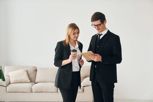 Young guys standing with woman indoors near sofa agaist white wall.