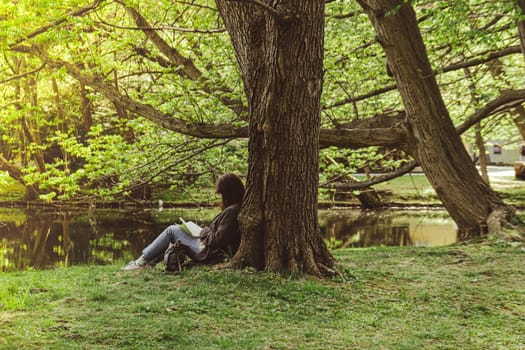 Attractive young woman reading book while sitting on grass in green public park. Springtime outdoors. Greenery unity with nature. Spend free time on open air. Education concept