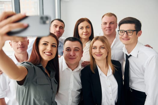 Makes selfie. Group of people in official formal clothes that is indoors in the office.