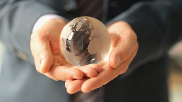 Businessman in suit holding glass globe with world map closeup. International financial relations concept