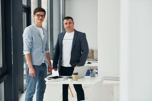 Young guy with adult man standing indoors in the office together.