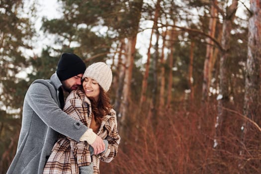 Cheerful couple have a walk in the winter forest at daytime.