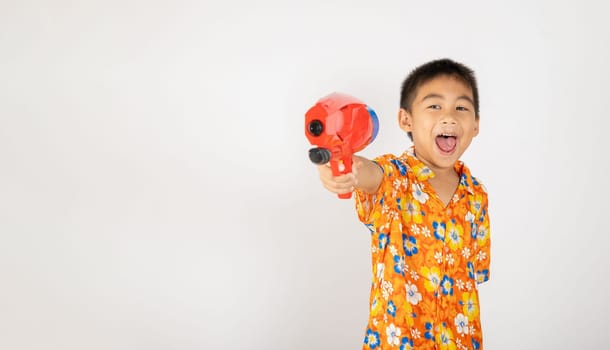 Happy Songkran Day, Asian kid boy with floral shirt hold water gun, Thai child funny hold toy water pistol and smile, isolated on white background, Thailand Songkran festival national culture concept