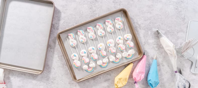Flat lay. Unbaked unicorn theme meringue pops on a baking sheet lined with parchment paper.
