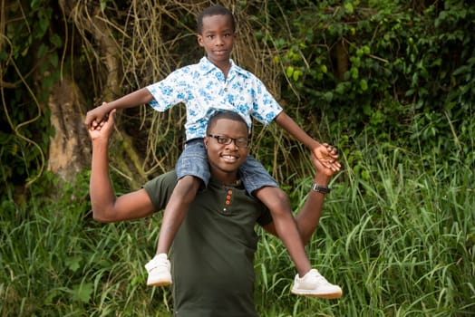 young man in green tee-shirt standing with his child on shoulders smiling on camera.