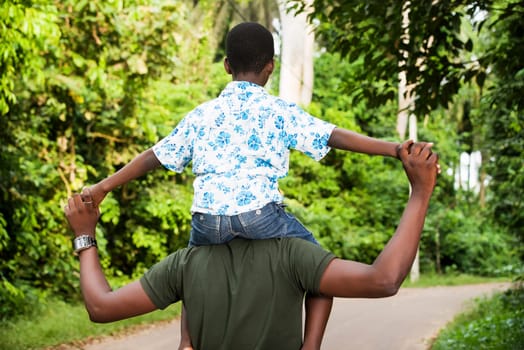 a young man standing in a park with his son on his neck giving back to the camera.