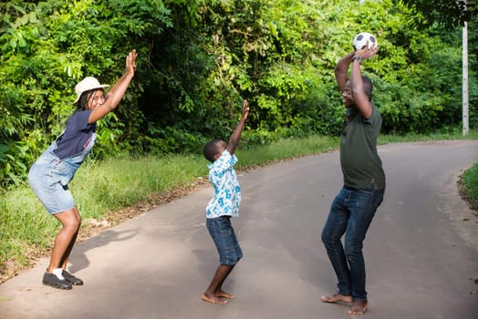 a family standing in a park playing ball with their son laughing.