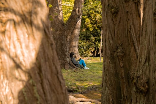 Attractive young woman reading book while sitting on grass in green public park. Springtime outdoors. Greenery unity with nature. Spend free time on open air. Education concept