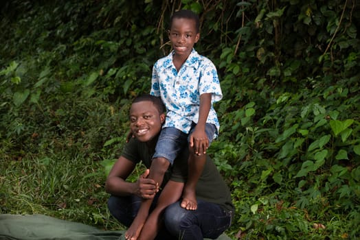 a young man crouched in a park carrying his son on the shoulder looking at the camera smiling.