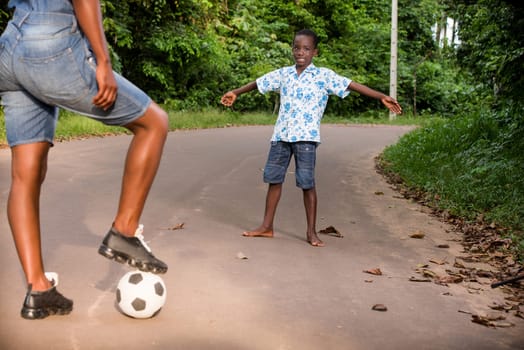 a child standing outside is waiting for his mother to give him the ball while smiling.
