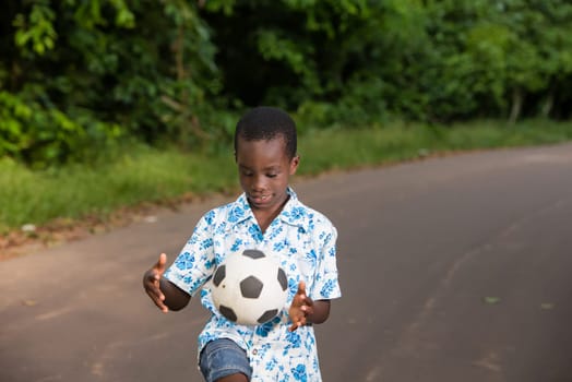 young boy standing outdoors playing ball with a smile.