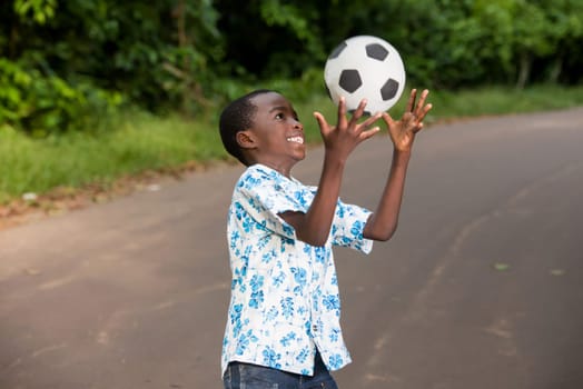 young boy standing outdoors playing ball with a smile.