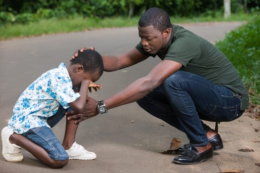 a young man crouched in a park air to calm his son who is crying.