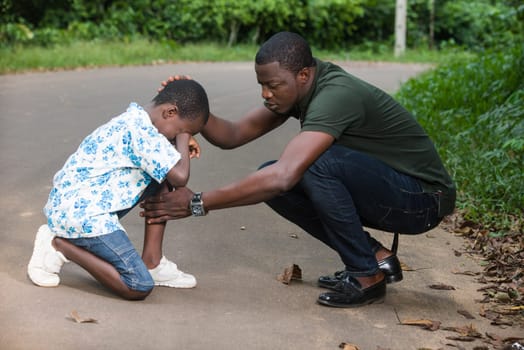a young man crouched in a park air to calm his son who is crying.