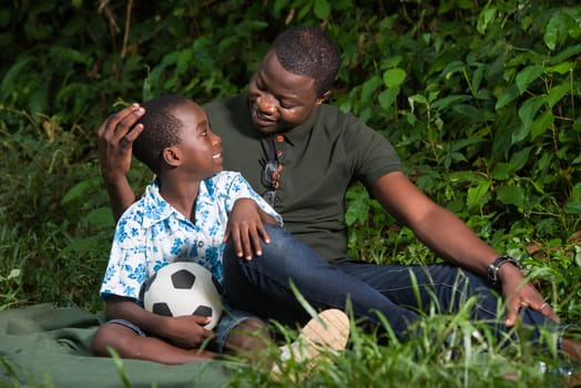 a young man sitting in a park with his son and looking at each other with a smile.