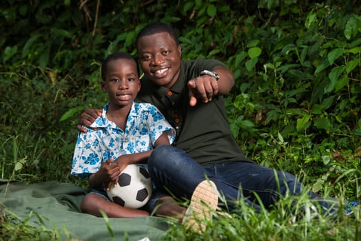 a young man sitting in a park with his son and showing him something with a smile.