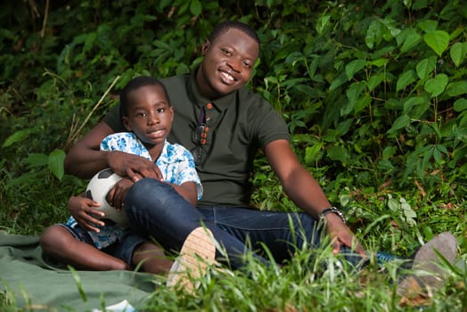 a young man sitting in a park with his child and look at the camera smiling.