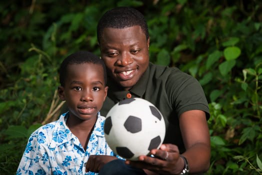 a young family sitting in a park with a ball smiling.