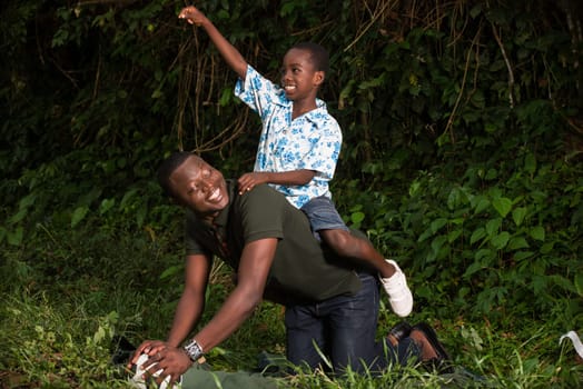 a young boy on his father's back in a park laughing with his fist raised.