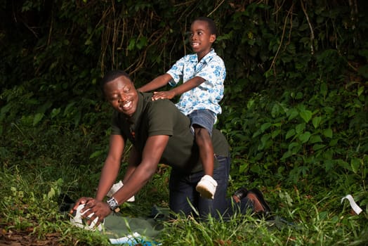a young boy on the back of his father in a park smiling.
