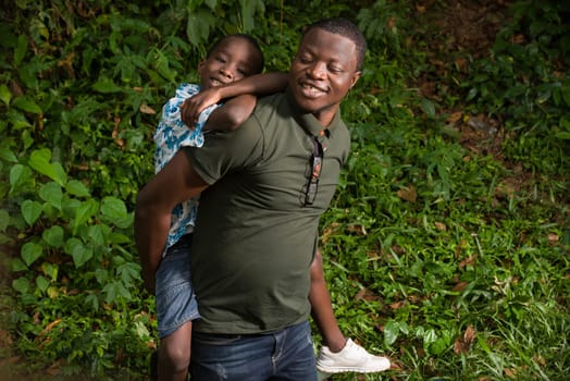 a young man kneeling in a park with his child on his back smiling.