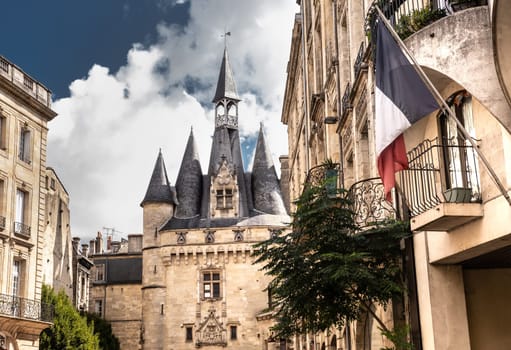 Old gate entrance to the city of Bordeau and French flag . Beautiful sightseeing buildings in the center of Bordeaux, France.