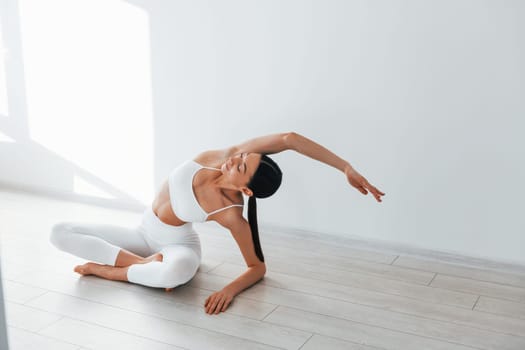 Doing yoga. Young caucasian woman with slim body shape is indoors at daytime.