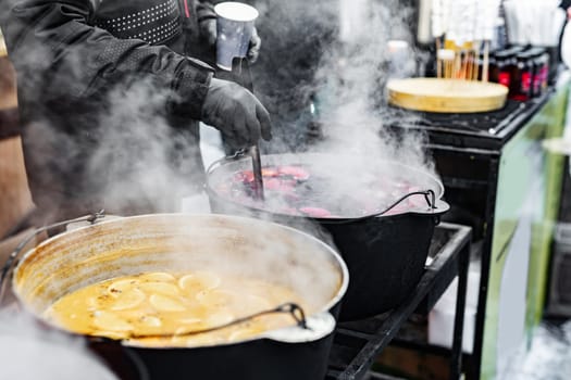 Beverages fruits and berries hot mulled wine in pots with steam in street food market. Colorful hot sweet drinks at fair festival outdoors closeup
