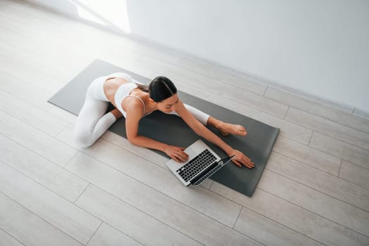 On yoga mat. Young caucasian woman with slim body shape is indoors at daytime.