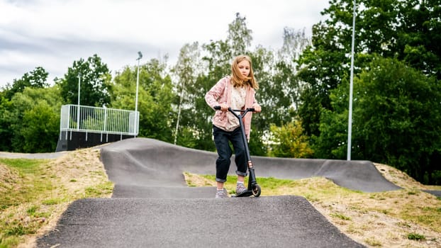 Preteen girl riding scooter in the park. Cute female child with eco vehicle outdoors