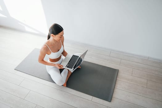 On yoga mat. Young caucasian woman with slim body shape is indoors at daytime.