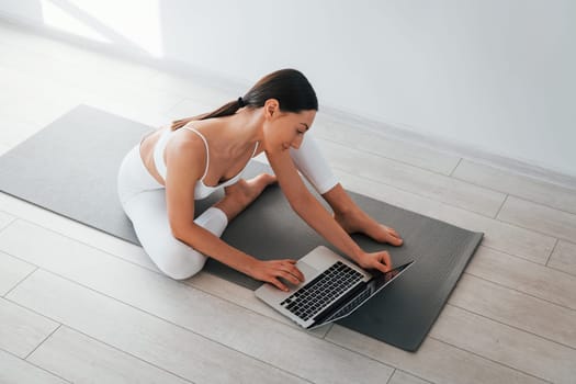 On yoga mat. Young caucasian woman with slim body shape is indoors at daytime.