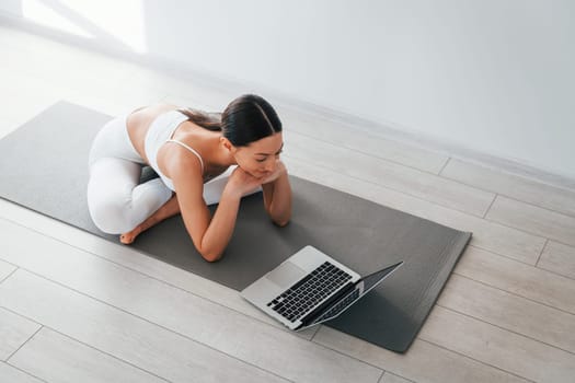 On yoga mat. Young caucasian woman with slim body shape is indoors at daytime.