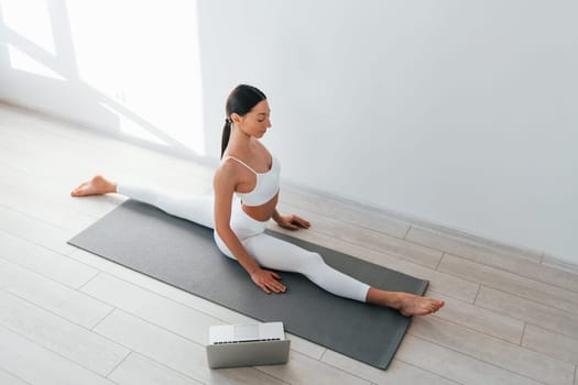 On yoga mat. Young caucasian woman with slim body shape is indoors at daytime.