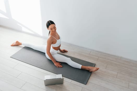 On yoga mat. Young caucasian woman with slim body shape is indoors at daytime.