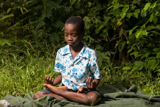 portrait of a child sitting on a piece of loincloth in the bush and meditating