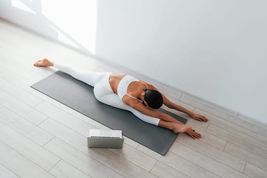 On yoga mat. Young caucasian woman with slim body shape is indoors at daytime.