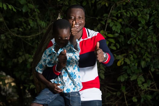 portrait of young smiling family standing against a tree trunk and gesturing to the camera