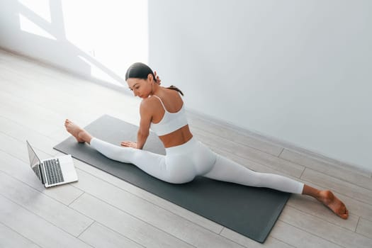 On yoga mat. Young caucasian woman with slim body shape is indoors at daytime.