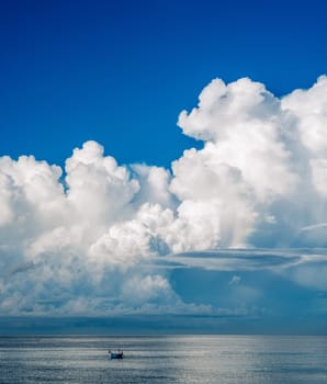 A boat is sailing in the ocean with a large cloud in the sky