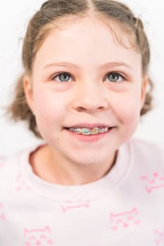 Little girl with rainbow braces smiling at the camera.