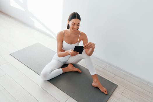 Holds phone in hands. Young caucasian woman with slim body shape is indoors at daytime.