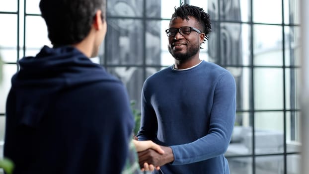 Diverse male colleagues in modern office corridor, young african american and caucasian business people discussing common project work, meeting in company work