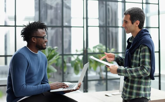 Young businessman holding laptop while discussing new project with african american colleague