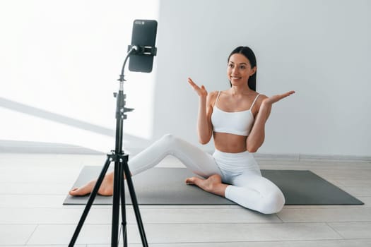 Phone is recording video. Young caucasian woman with slim body shape is indoors at daytime.