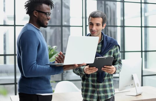 Two cheerful businessmen discussing something on the laptop in an office