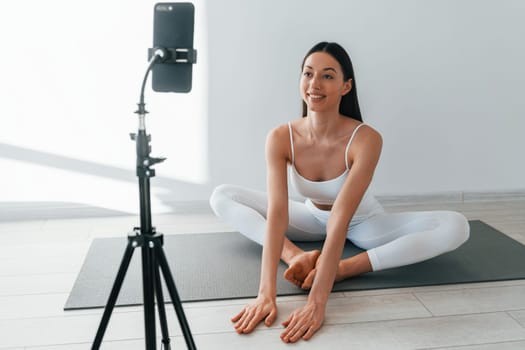 Phone on tripod. Young caucasian woman with slim body shape is indoors at daytime.