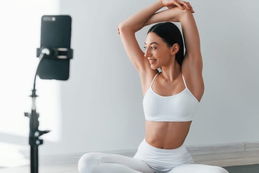 Phone on tripod. Young caucasian woman with slim body shape is indoors at daytime.