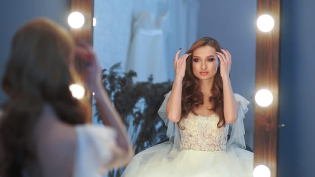 Beautiful girl model in wedding dress posing in front of a mirror