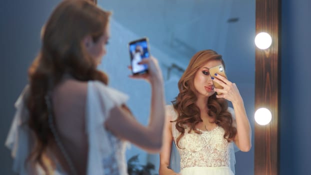 Beautiful girl model posing in front of a mirror and taking pictures on a smartphone